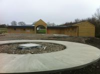 Large stable yard with a taller than standard archway, in an L-shaped design. Concrete ready for a walker in foreground of picture.